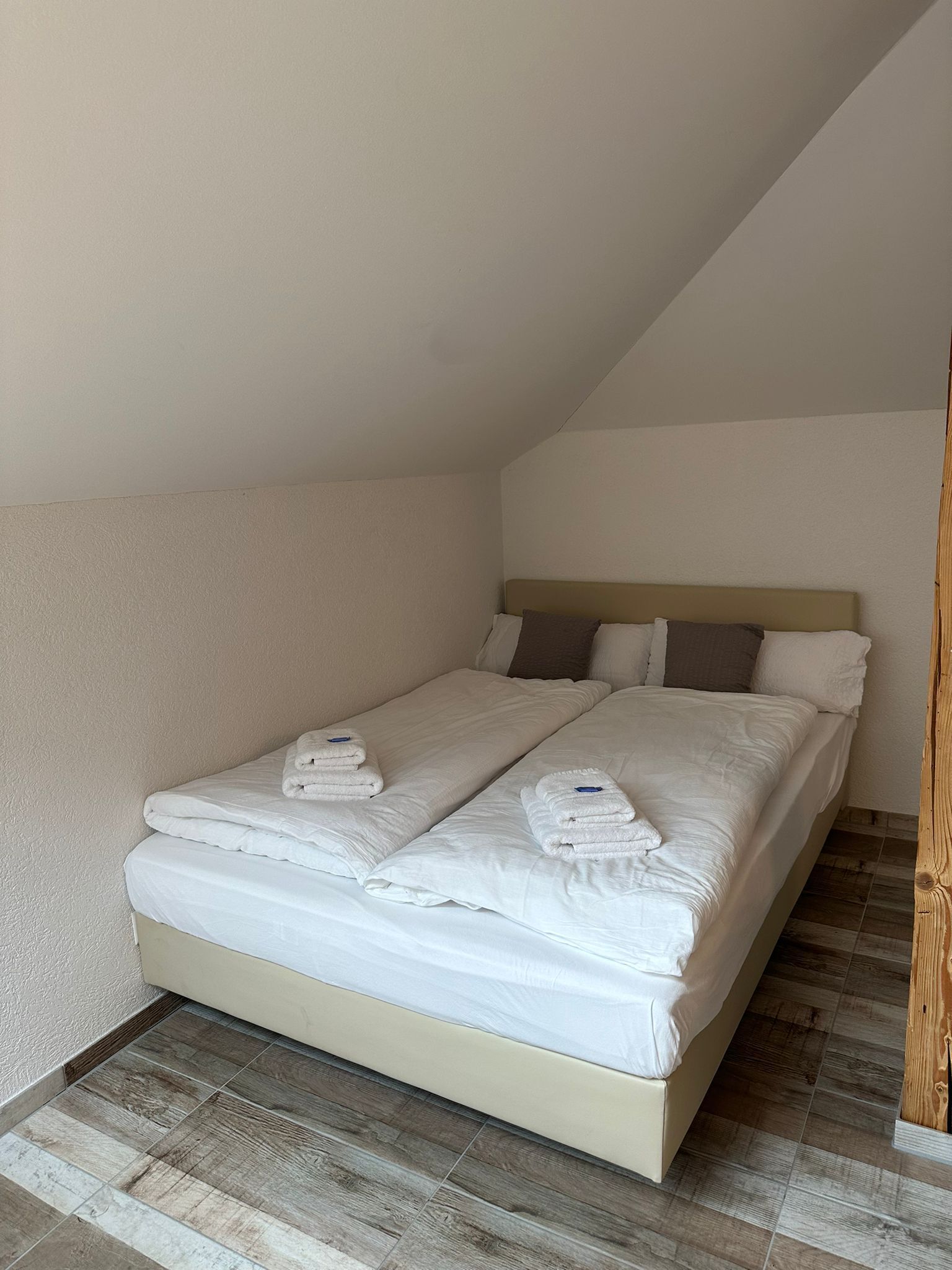 A single bed with white linens and towels, a wooden headboard, and a sloped ceiling.