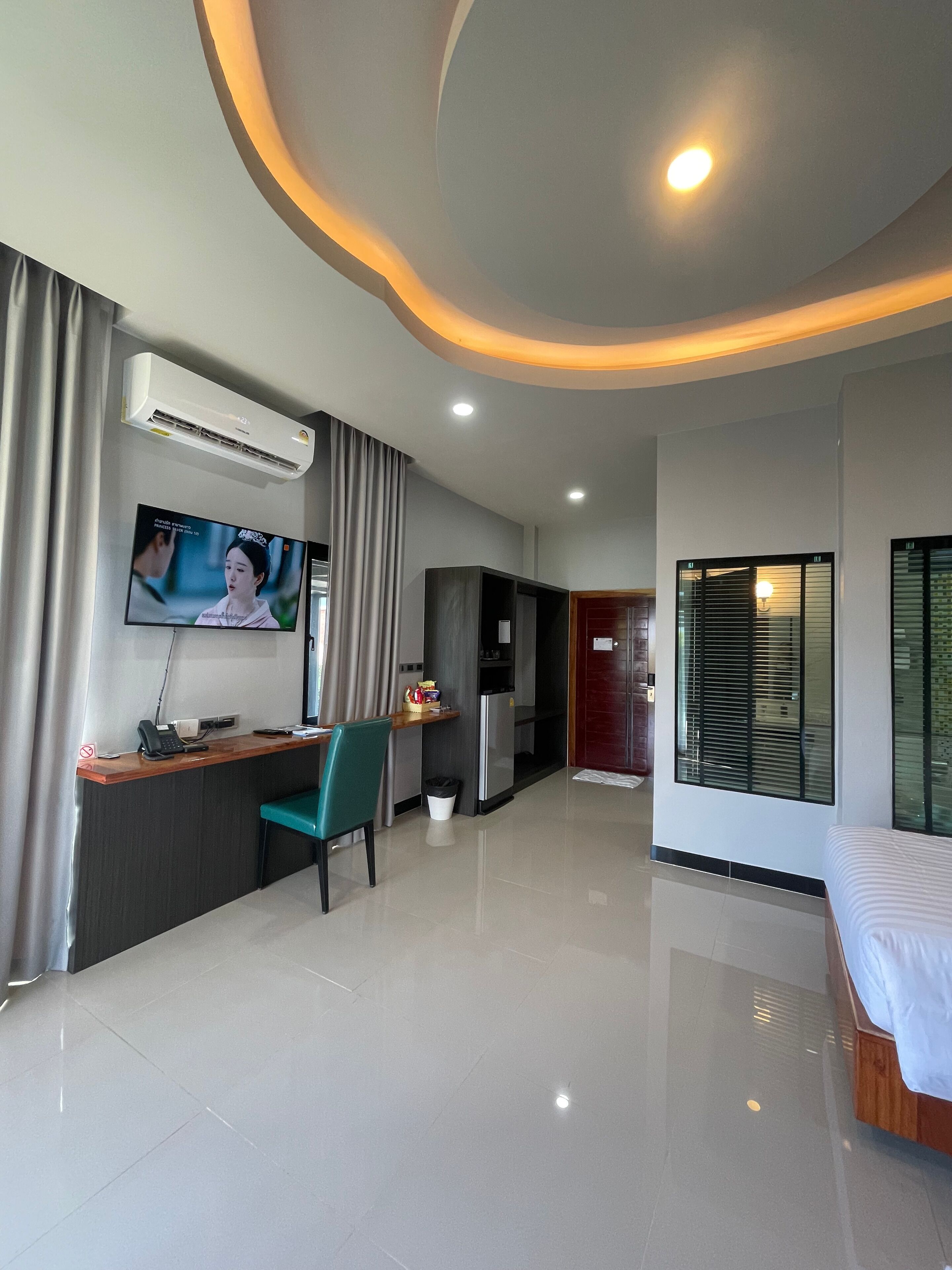 Una habitación de hotel moderna con televisión de pantalla plana, un escritorio con silla, una cama y un ventanal con persianas.