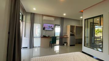 A modern hotel room with a large bed, a desk with a computer, a TV, and a view of the outdoors.