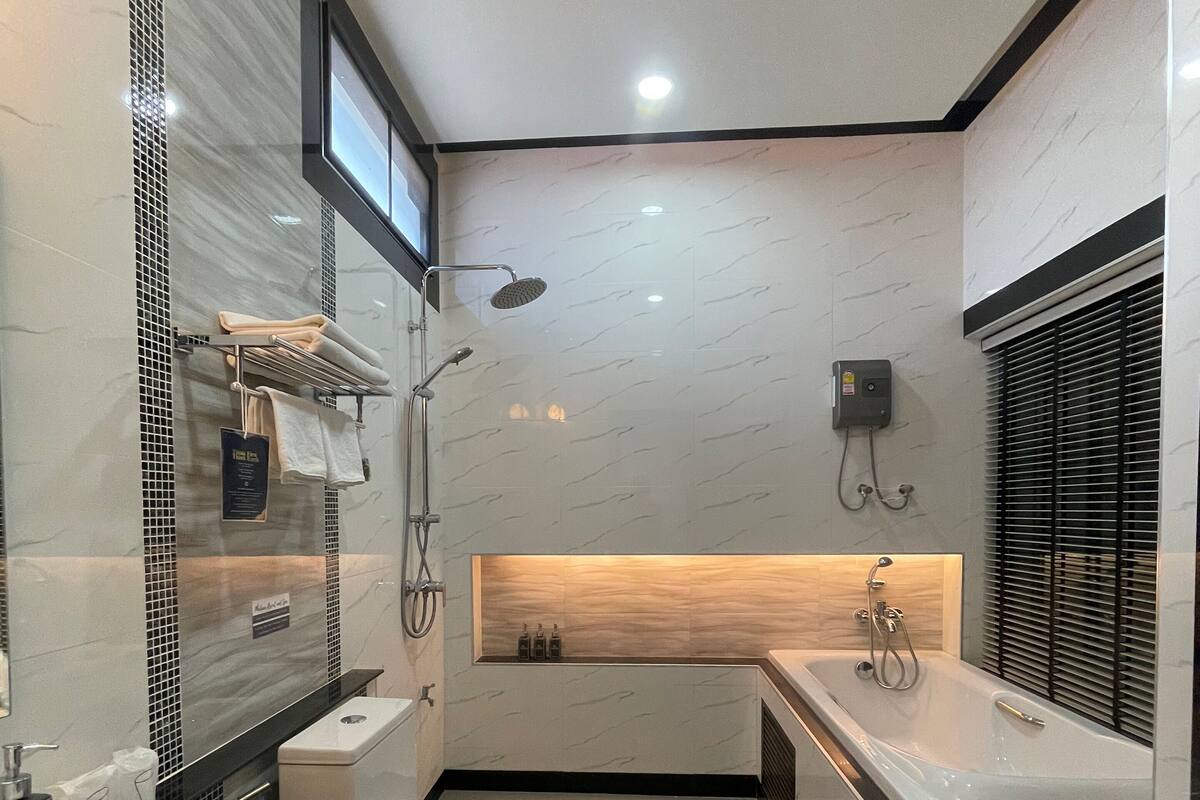 A modern bathroom with a large mirror, two sinks, a shower, and a toilet.