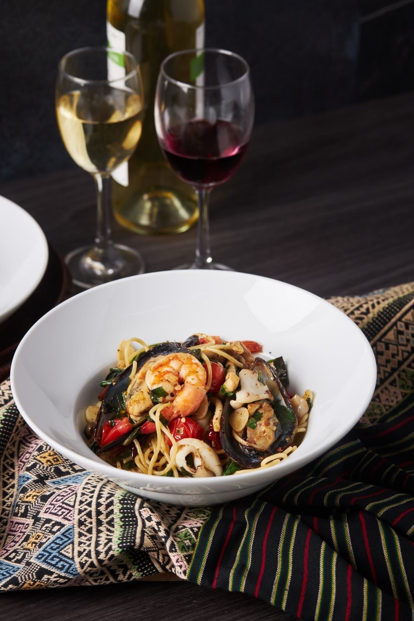 Un plato de pasta con camarones y mejillones, acompañado de copas de vino.