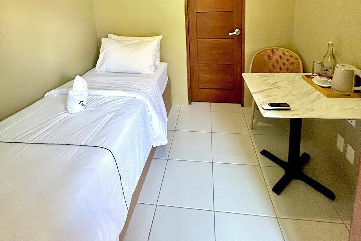 A small, clean room with a bed, a wooden door, a small table with a tray, and a chair.
