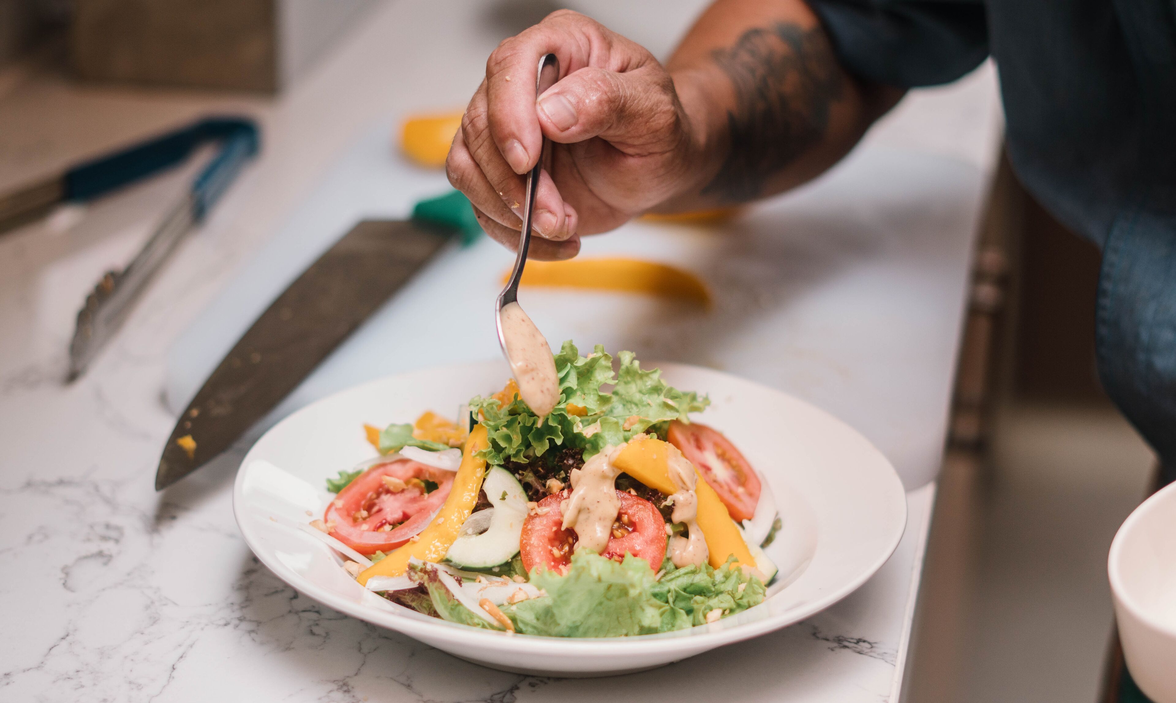 A person preparing a salad with a variety of vegetables and a creamy dressing.