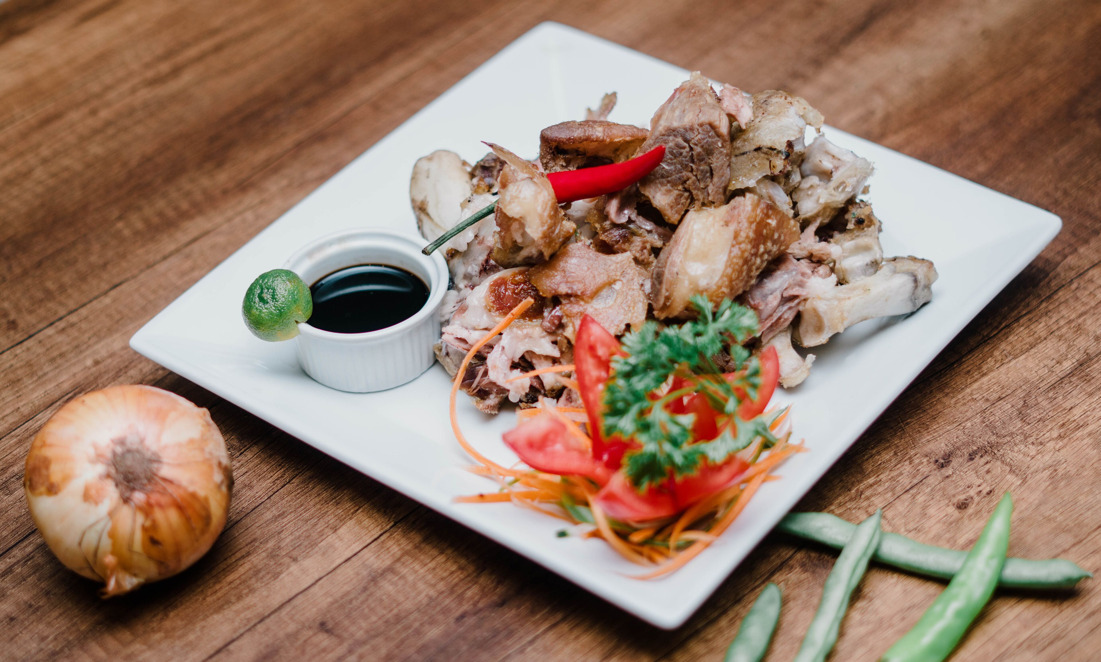 A plate of sliced meat with a side of sauce, garnished with vegetables and a chili pepper.