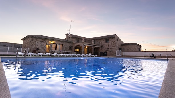 A swimming pool with lounge chairs and a stone building in the background.