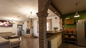 A modern kitchen with a brick fireplace, a stainless steel refrigerator, and a dining area with a green wall and wooden cabinets.