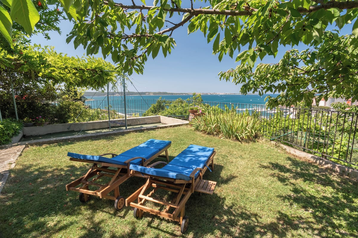 A backyard with two wooden lounge chairs and a view of the sea.