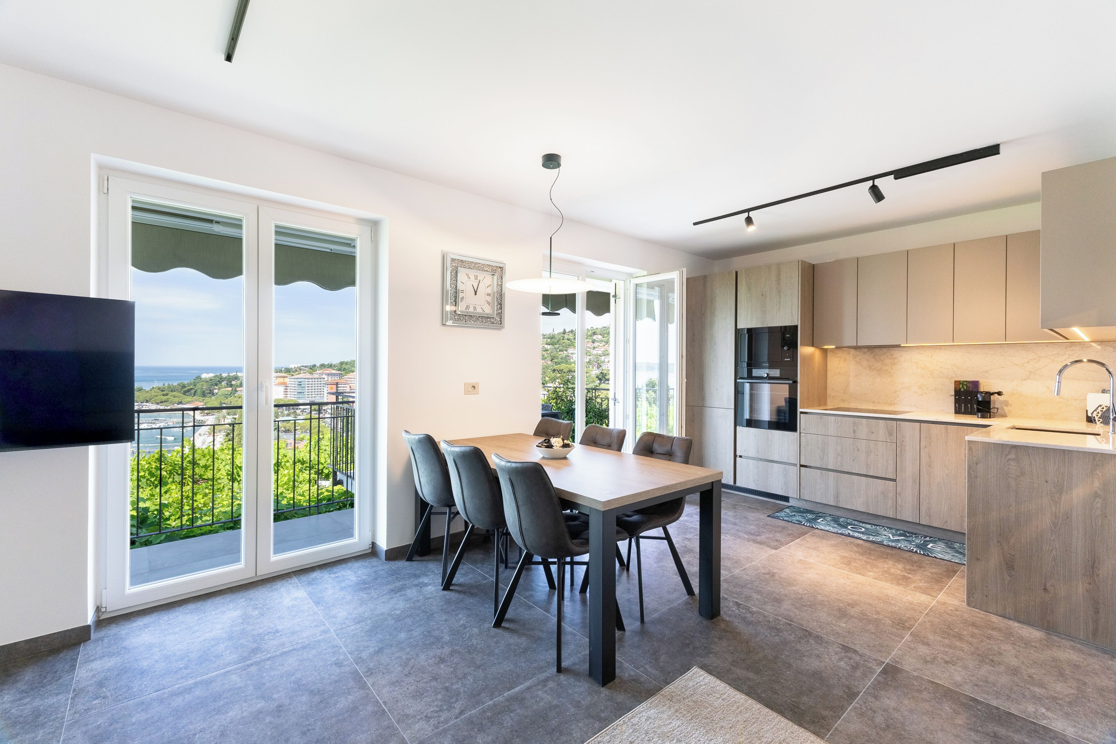 A modern kitchen with a dining area, large windows, and a flat-screen TV.