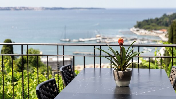 Un balcon avec une table et des chaises, offrant une vue sur la côte, avec des bateaux et de la végétation.