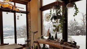 A rustic interior with a wooden table, hanging plants, and a view of a snowy landscape through large windows. - TERRALUNA - Holiday home surrounded by the greenery of San Leo, San Marino and Montefeltro (San Leo)