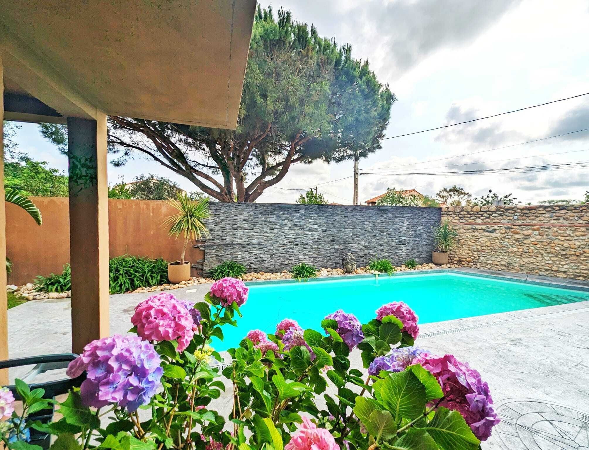 Une piscine avec un mur en pierre et un arbre en arrière-plan.