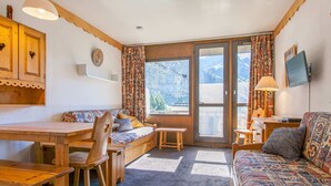 Ein gemütliches Zimmer mit einer hölzernen Bank, einem Sofa und einem Tisch. Ein Fenster mit Vorhängen bietet Blick auf Berge.