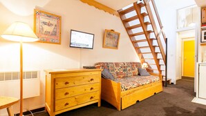 Ein gemütliches Zimmer mit einem Holzkasten, einem gemusterten Sofa, einem Fernseher und einer Holzleiter.