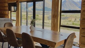 A spacious room with a large wooden dining table and chairs, large windows offering a view of mountains. - Log cabin - beautiful, relaxing getaway with breathtaking views! (Lake Ōhau)