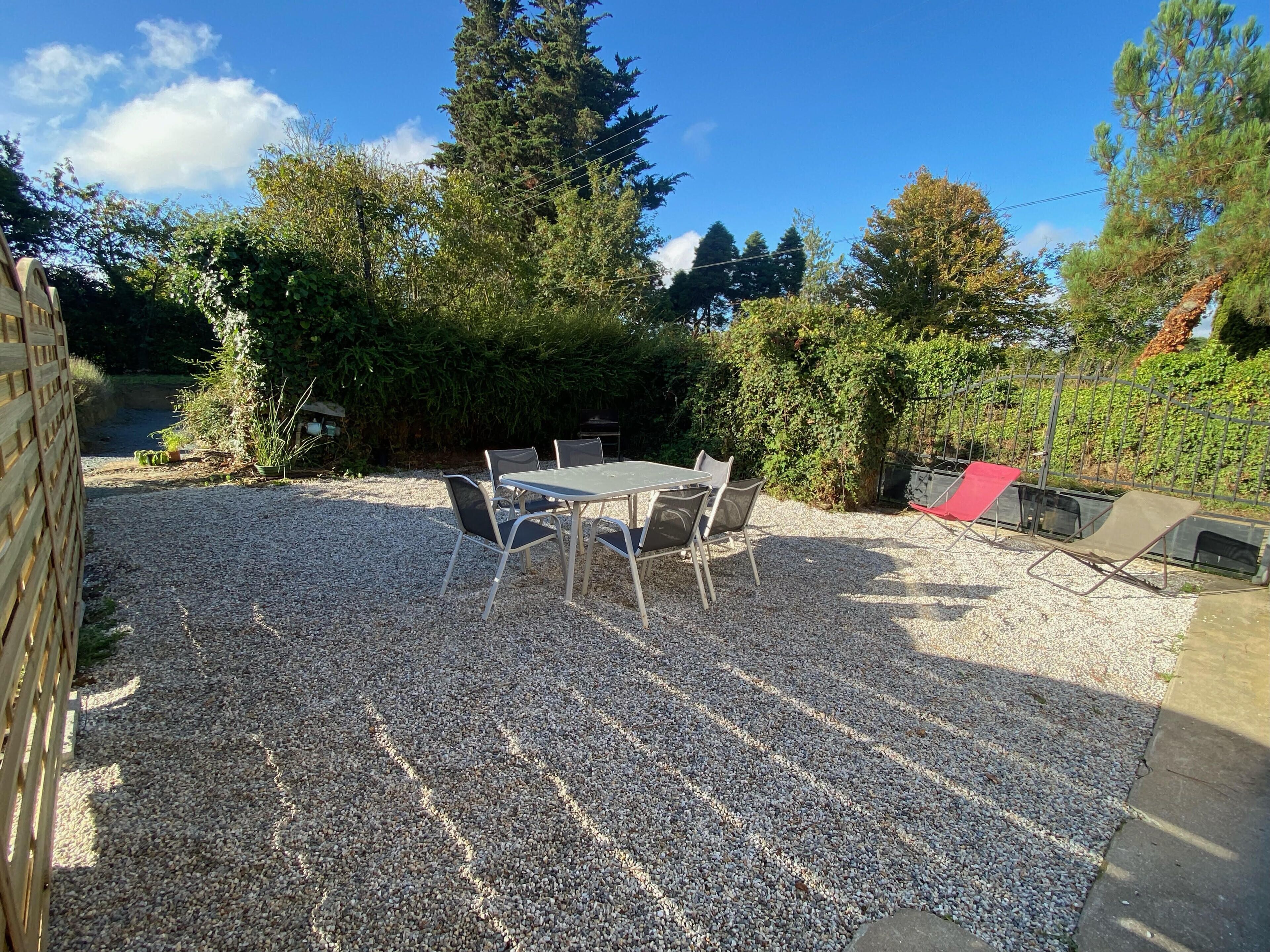 Un espace patio avec un sol en gravier, une table ronde entourée de chaises et un fauteuil de jardin rouge.