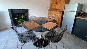 Un comedor con mesa de vidrio y cuatro sillas, un armario de madera, un refrigerador y una chimenea.