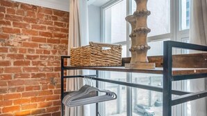 Huoneessa on tiiliseinä, ikkunassa on verhot, metallinen kerrossänky, jossa on säilytystilaa, lamppu ja näkymä kadulle.