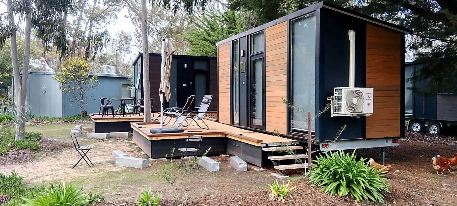 A modern, compact cabin with a deck, outdoor seating, and a large fan.