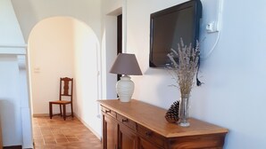 A hallway with a wooden cabinet, a chair, a table with a lamp, and a wall-mounted TV.