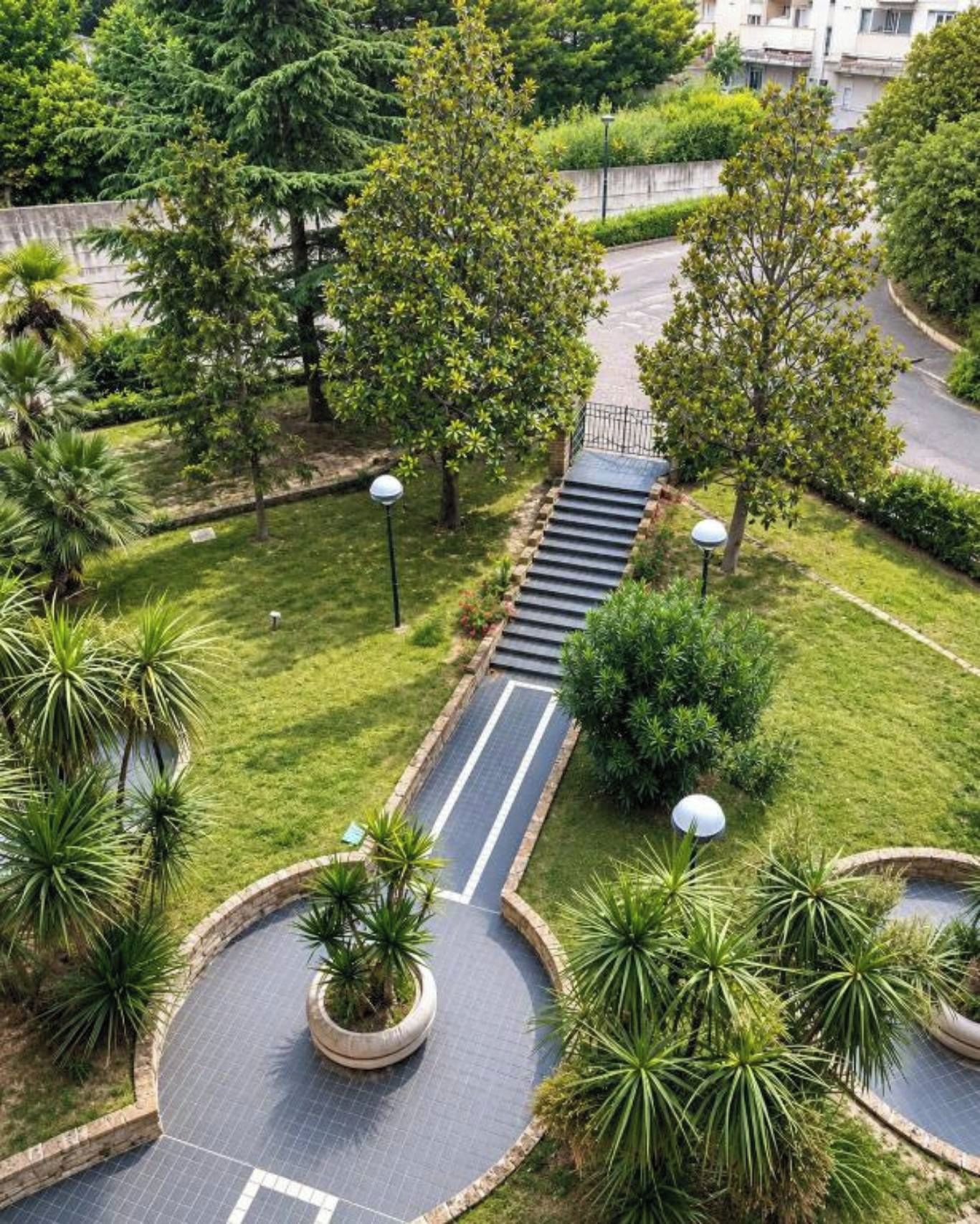 A landscaped area with a paved pathway, trees, and a small water feature.