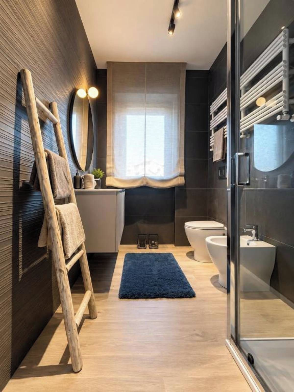 Un baño moderno con una escalera de madera, un espejo grande, un lavamanos, un inodoro y un bidé.