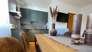 A modern kitchen with dark cabinets, a wooden dining table, and chairs. A vase with sticks is on the table, and a TV is mounted on the wall. - Cozy apartment clean and very bright equipped with all the comforts (Pescara)
