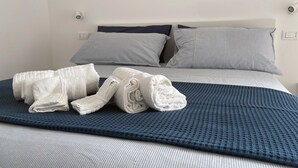 A neatly made bed with a blue textured bedspread, two pillows, and a pair of folded white towels. - Cozy apartment clean and very bright equipped with all the comforts (Pescara)