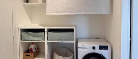 A laundry room with a washing machine, shelves with storage bins, and a hanging laundry rack.