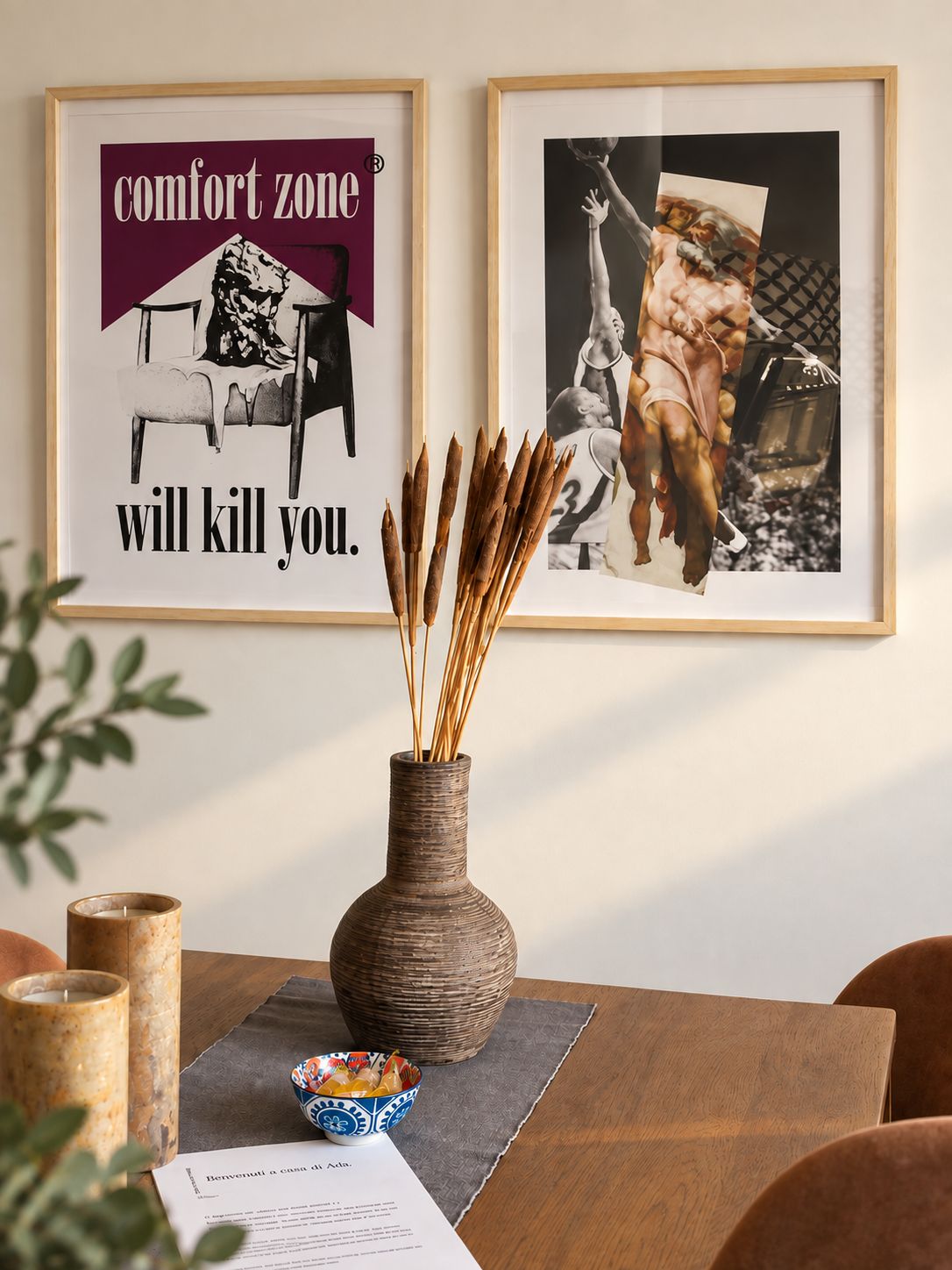 A framed poster with a bold statement, a vase with reeds, a candle, and a bowl on a table.