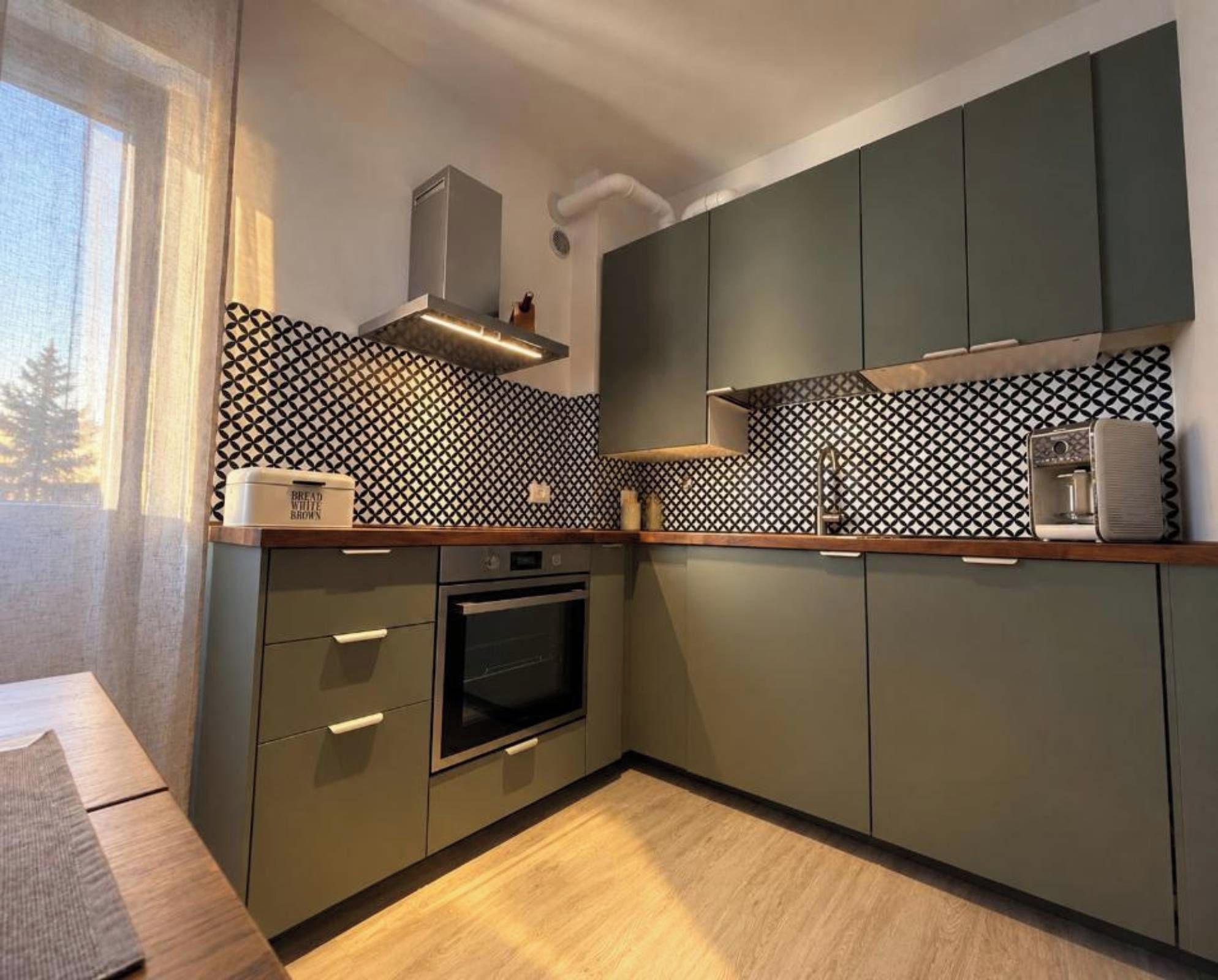 A modern kitchen with a built-in oven, a coffee machine, and a patterned backsplash.