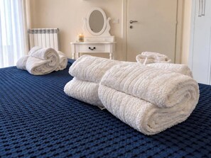 Ein ordentlich bezogenes Bett, gerollte weiße Handtücher, eine weiße Kommode mit Spiegel und eine Tür in einem Hotelzimmer.