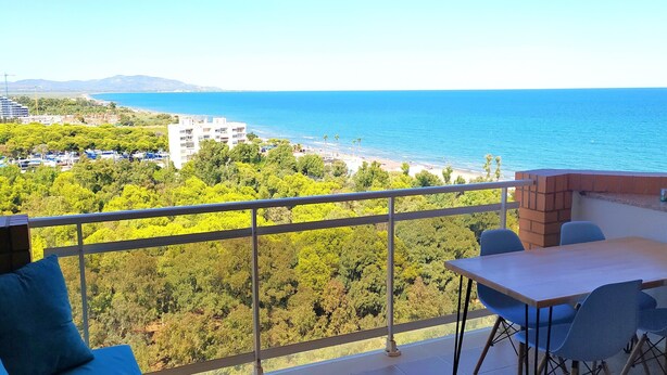 Un balcon avec une table et des chaises, donnant sur une plage et une zone boisée.