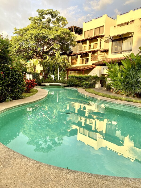 A swimming pool surrounded by lush greenery and a multi-story building with balconies.