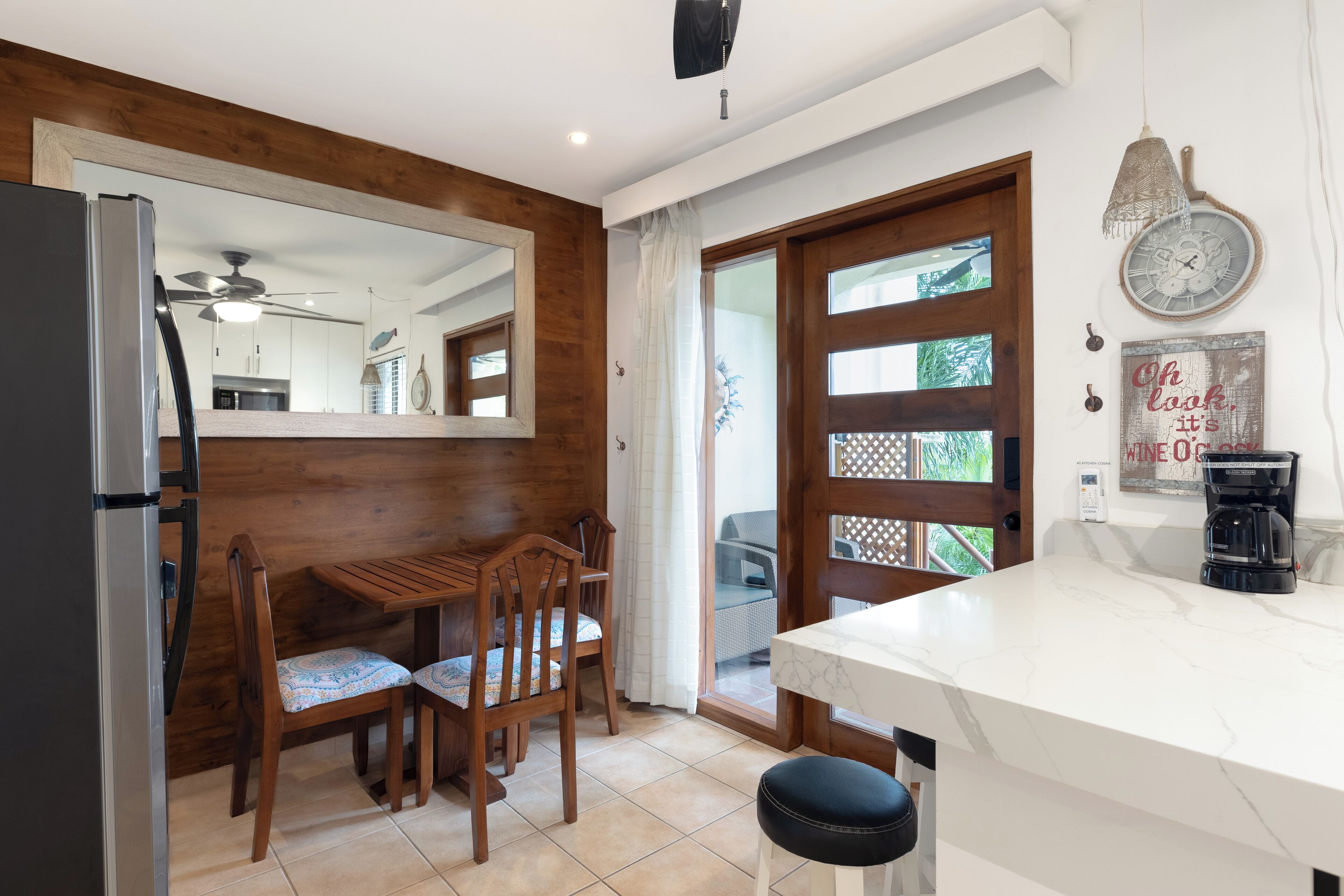 A modern kitchen with a wooden dining area, a refrigerator, a coffee maker, and a clock on the wall.