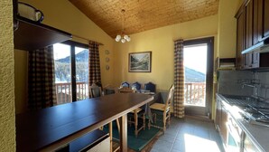 Une cuisine chaleureuse avec des meubles en bois, un coin repas avec une table et des chaises, et une vue sur les montagnes par les fenêtres.