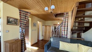 Un salon chaleureux avec un plafond en bois, un canapé bleu, des rideaux à carreaux et un escalier.