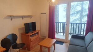 Ein Wohnzimmer mit Fernseher auf einem Holzständer, einer Couch, einem Esstisch und einem Stuhl.