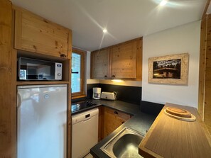 A compact kitchen with wooden cabinets, a microwave, a coffee maker, and a sink.
