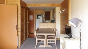 A compact room with a wooden dining table and chairs, a small kitchenette with a microwave and refrigerator, and a TV on a stand. - 3-Room Apartment · Ski-In/Ski-Out · Balcony · 7 ppl (Belle Plagne)