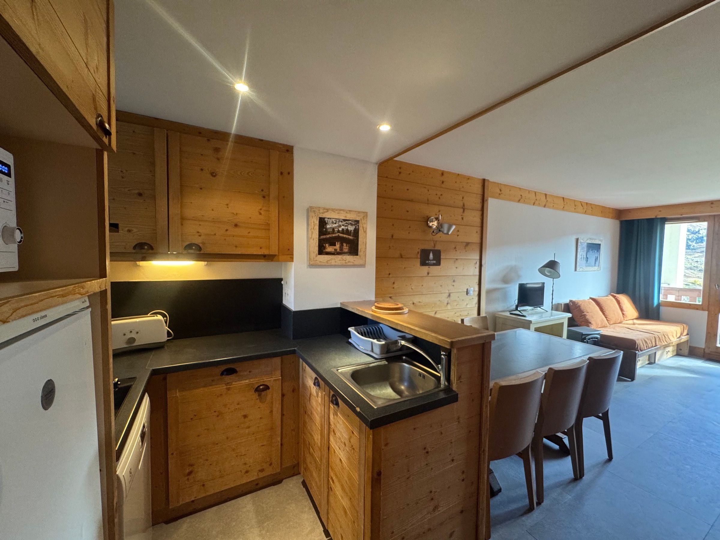 Een praktische keuken met houten kastjes, een inbouweiland met een spoelbak, en een eethoek met stoelen.