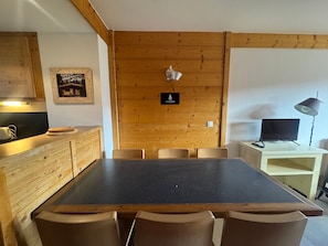 Ein Zimmer mit Holzwandverkleidung, einem Esstisch, Stühlen, einem Fernseher und einer Lampe.