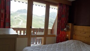 A bedroom with a large window, wooden headboard, and a white quilted bedspread. - 3-Room Apartment · Ski-In/Ski-Out · Balcony · 7 ppl (Belle Plagne)