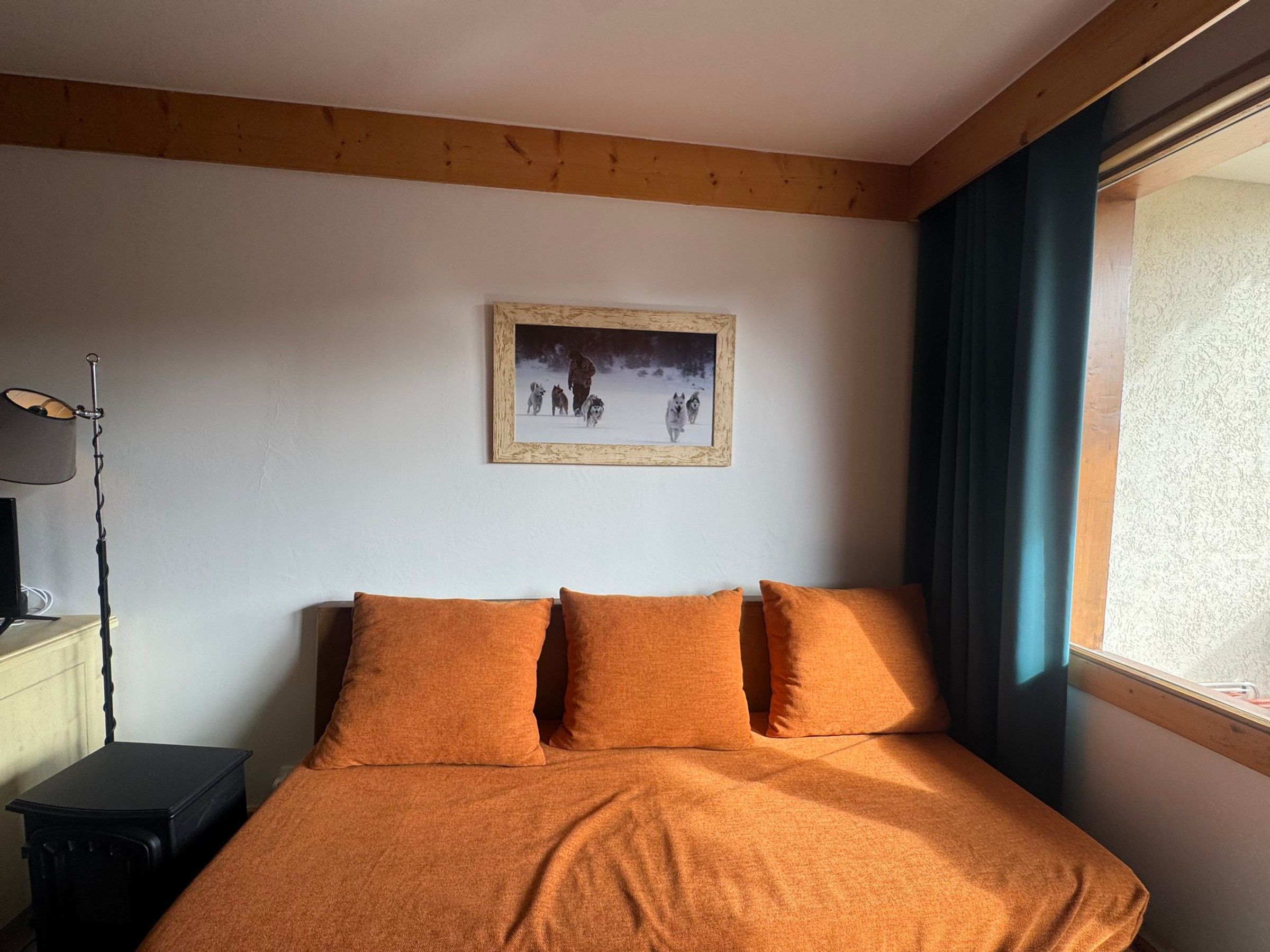 Una camera da letto con un letto, un quadro appeso al muro, una lampada e una finestra con tende.