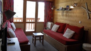 A cozy room with a wooden wall, a sofa, a small table, and a television. - 3-Room Apartment · Ski-In/Ski-Out · Balcony · 7 ppl (Belle Plagne)