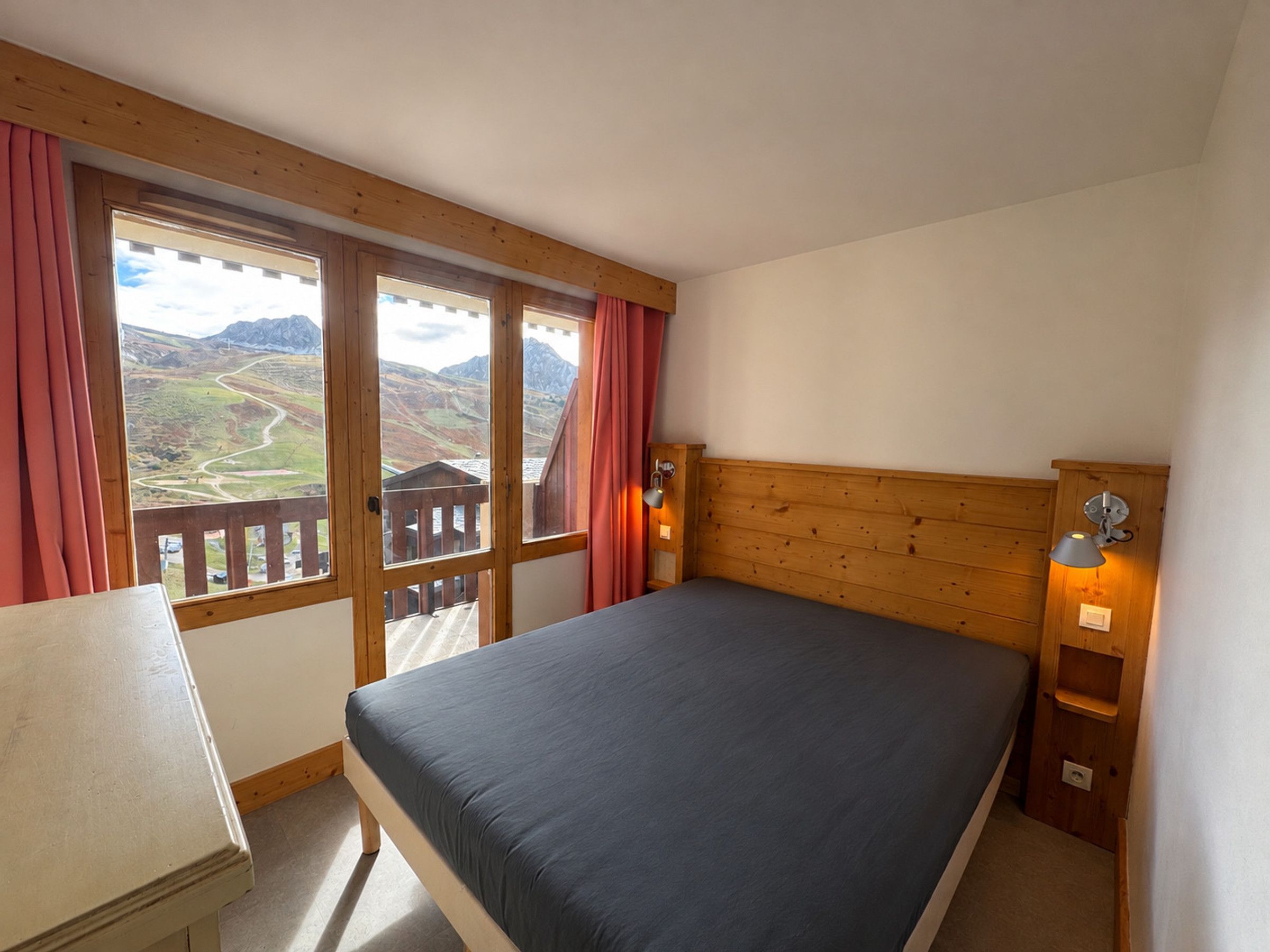 A bedroom with a bed, wooden headboard, a nightstand, a lamp, and a window with curtains.
