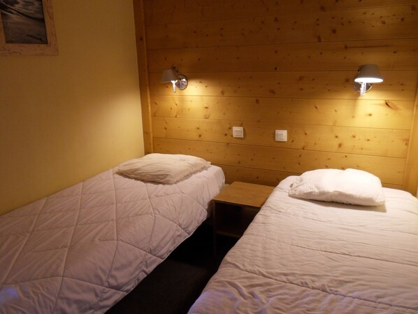 Una habitación con dos camas individuales, cada una con un cojín y cabecera. Hay apliques de luz fijos en las paredes a cada lado de las camas.