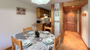 A dining area with a table set for four, wooden chairs, a chandelier, and a kitchen in the background.