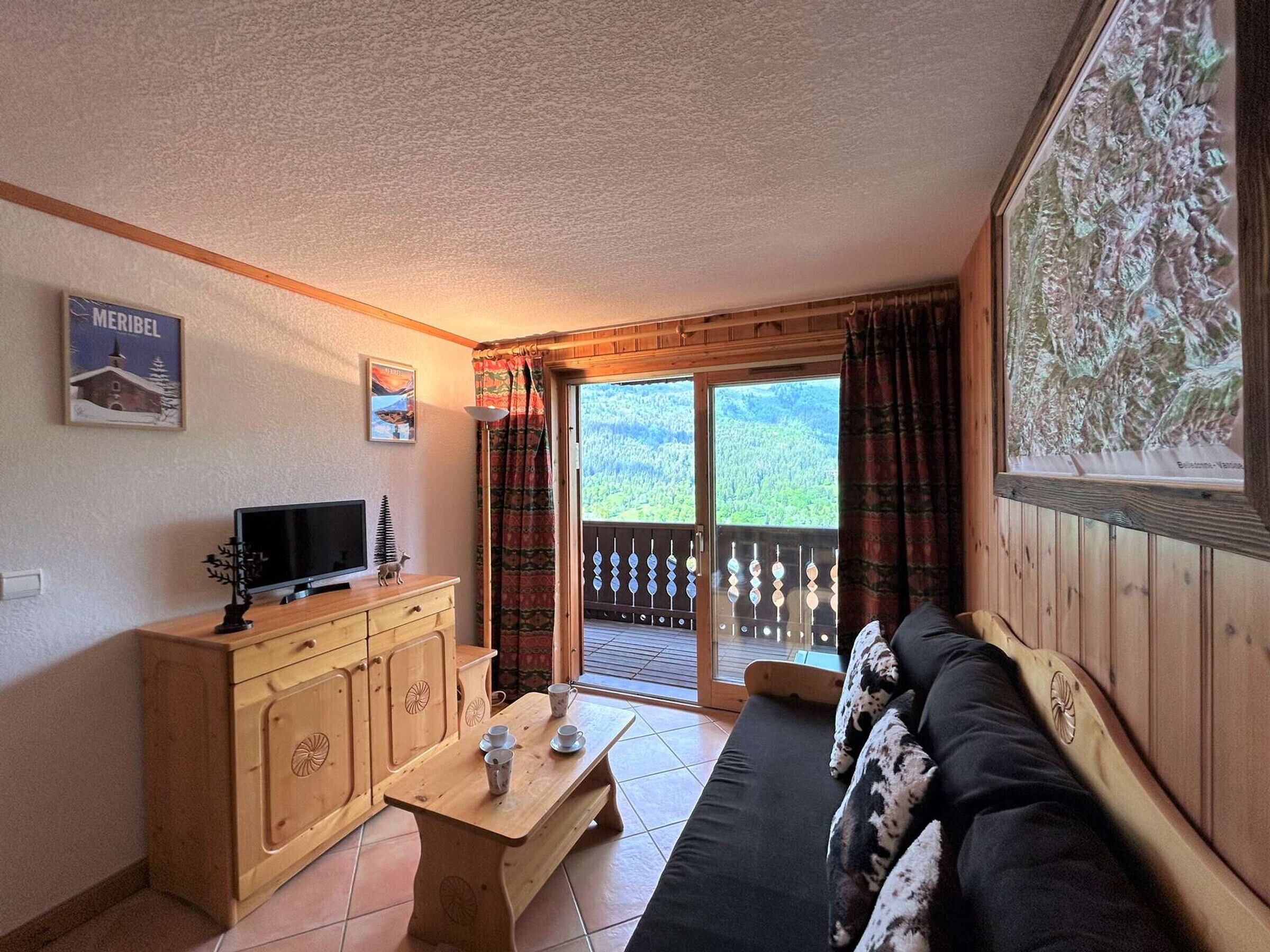 A cozy living room with a wooden sofa, a TV on a wooden cabinet, and a balcony with a scenic view.