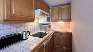 A compact kitchen with wooden cabinets, a gas stove, a microwave, and a kettle.