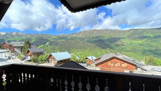 A mountain view from a balcony with a wooden railing and a clear sky.